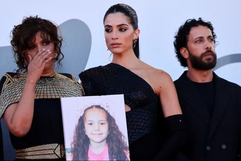 Kaouther Ben Hania, Motaz Malhees e Saja Kilani com a foto de Hind Rajab — Foto: REUTERS/Yara Nardi Kaouther Ben Hania, Motaz Malhees e Saja Kilani com a foto de Hind Rajab — Foto: REUTERS/Yara Nardi